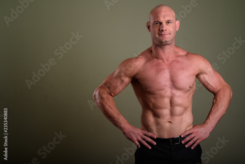 Bald muscular man shirtless against colored background