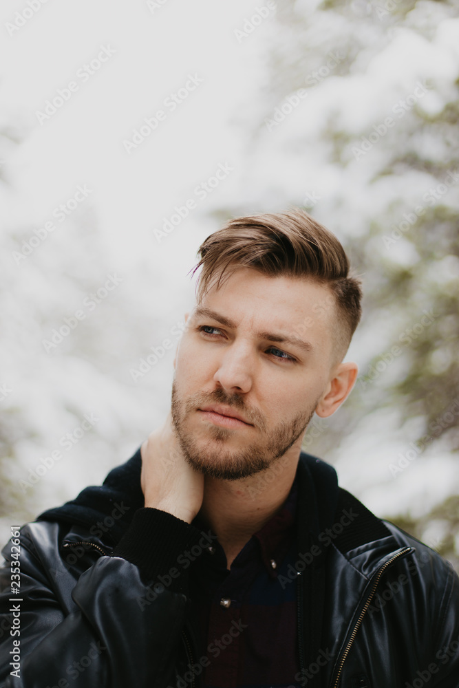 Portrait of Attractive Trendy Modern Young Male Model Smiling and Enjoying the Outdoors and the White Winter Snow in the Tree Canopy While Posing in Fashionable Leather Bomber Jacket Portrait of Attractive Trendy Modern Young Male Model Smiling and Enjoying the Outdoors and the White Winter Snow in the Tree Canopy While Posing in Fashionable Leather Bomber Jacket