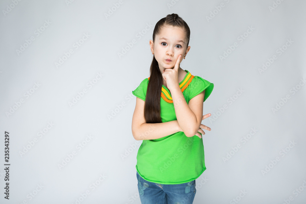 Girl on a gray background put her finger to her cheek. Girl on a gray background put her finger to her cheek.