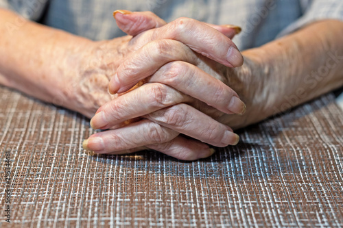 The hands of an elderly woman resting on the table. Parkinson.