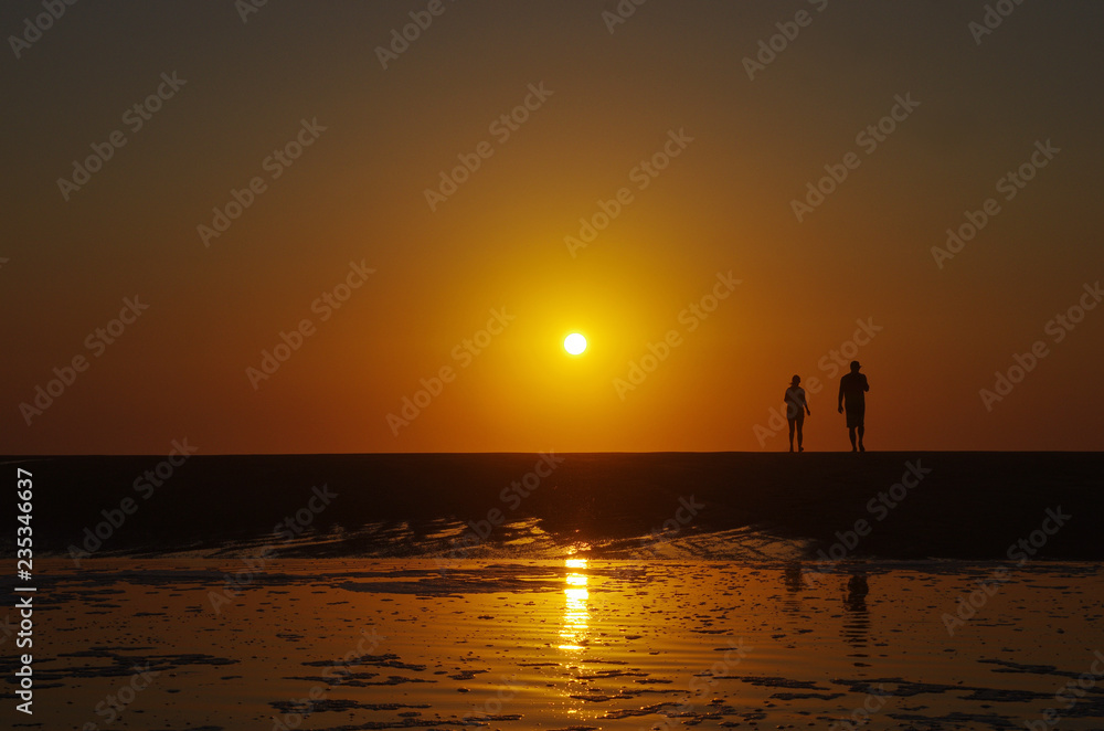 Obraz premium Silhouette of a couple walking on the beach, sunset in the background. Beautiful beach sunset. Holiday happiness.