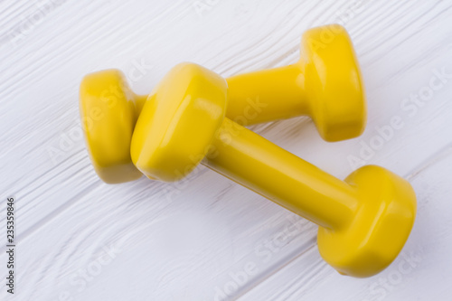 Pair of yellow dumbells on white wood background. Hand weights on wooden surface. Fitness equipment background.