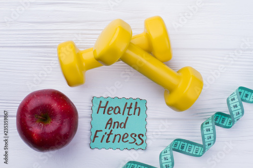 Yellow dumbbells, red apple and measuring tape. Healthy eating and fitness. Healthy food and sport.