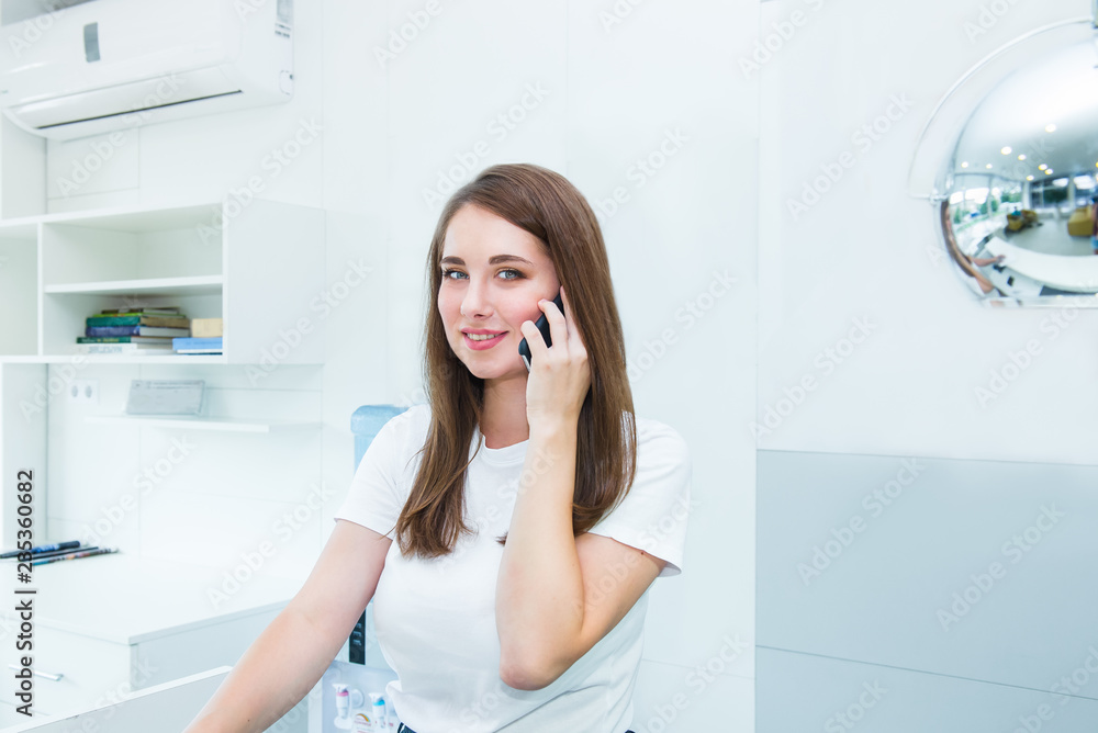 Portrait of smiling friendly young woman looking at camera, talking on phone. Administrator. manager in the office, clinic, center, hotel. Occupation concept. Selective focus, space for text Portrait of smiling friendly young woman looking at camera, talking on phone. Administrator. manager in the office, clinic, center, hotel. Occupation concept. Selective focus, space for text