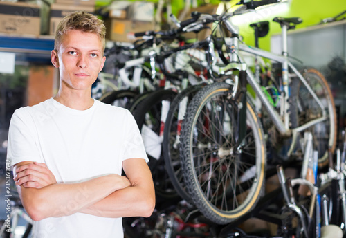 young serious male standing near the cycle in the shop