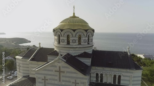 A large beautiful church on the bank of a river near the city. Shot. Fascinating riverside aerial view of the church with the city and parks background. photo