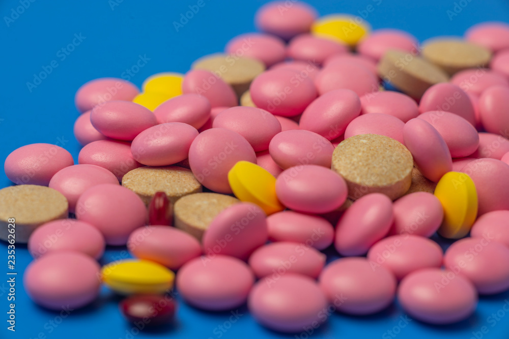 Multicolored medical tablets, pills, vitamins, close up on blue background Multicolored medical tablets, pills, vitamins, close up on blue background