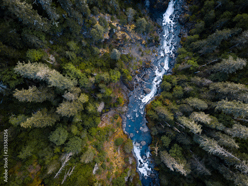 Aerial drone view looking down at a pristine blue mountain river running through the tall trees of the forest