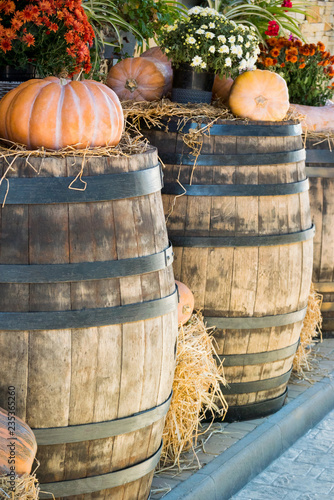 Vertical photo of old wooden barrels on which there are pumpkins and bouquets of wild flowers