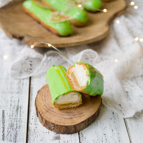 Eclair cut with tangerine jelly, orange mousse and mascarpone cream decorated with green icing and gold lace decoration on wooden plate. The concept of Christmas and New Year.Closeup, selective focus