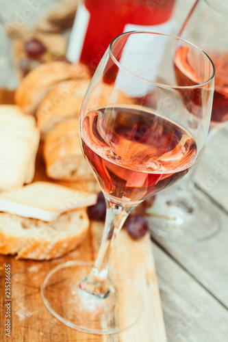 Two glasses of rose wine and board with fruits  bread and cheese on wooden table