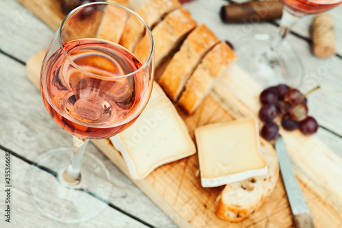 Two glasses of rose wine and board with fruits, bread and cheese on wooden table