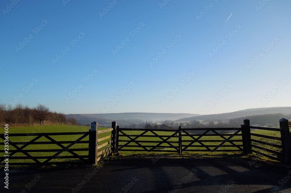 Beautiful misty fields of the Derbyshire Dales on a sunny winter day, with a wooden fence in the foreground and a vapor trail in the sky. Beautiful misty fields of the Derbyshire Dales on a sunny winter day, with a wooden fence in the foreground and a vapor trail in the sky.