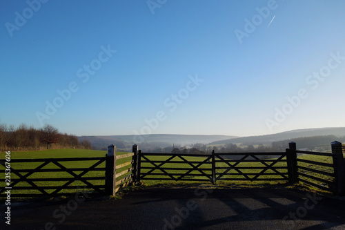 Beautiful misty fields of the Derbyshire Dales on a sunny winter day, with a wooden fence in the foreground and a vapor trail in the sky.