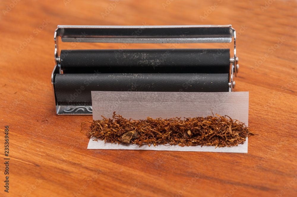 Brown hand rolling tobacco on the wood on paper and rolling machine Brown hand rolling tobacco on the wood on paper and rolling machine