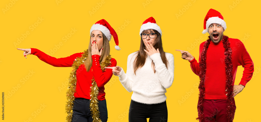 Fototapeta premium A group of people Blonde woman dressed up for christmas holidays pointing finger to the side with a surprised face on yellow background