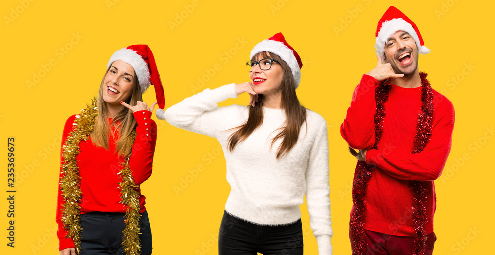 Fototapeta premium A group of people Blonde woman dressed up for christmas holidays making phone gesture. Call me back sign on yellow background
