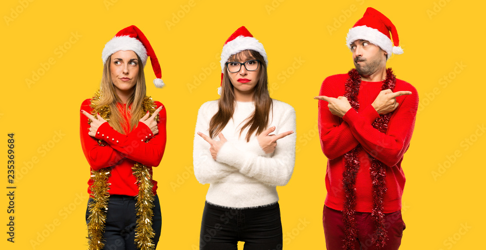 Fototapeta premium A group of people Blonde woman dressed up for christmas holidays pointing to the laterals having doubts. Undecided person on yellow background