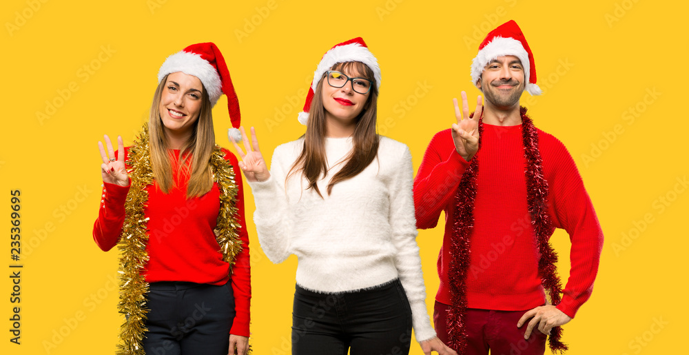 Fototapeta premium A group of people Blonde woman dressed up for christmas holidays happy and counting three with fingers on yellow background
