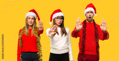 A group of people Blonde woman dressed up for christmas holidays making stop gesture with her hand denying a situation that thinks wrong on yellow background