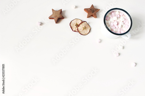 Christmas corner composition. Hot chocolate in enamel mug. Marshmallow,wooden stars, dry apple fruit slicess on white wooden table background. Winter breakfast. Flat lay, top view. Empty space.