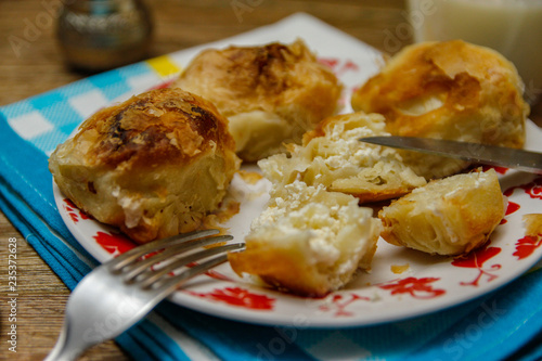 Traditional Bosnian pastry- manti borek with cheese on wooden table with yogurt. rustic background with low light and old bowls.