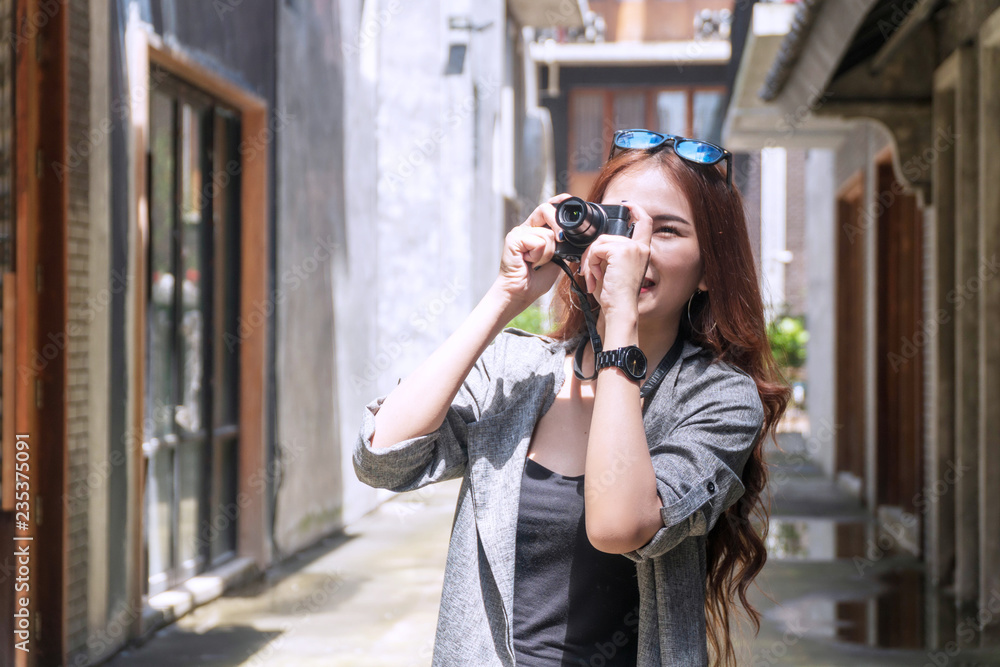 Cheerful photographer young woman with sunglasses holding camera taking photo in city. Traveler young girl use digital camera take photo reflex building while during travel. Photography concept.