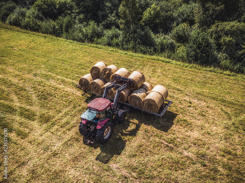 Aerial Drone Photo of Farmer Harvesting Hay Rolls in the Wheat Field with a Red Tractor