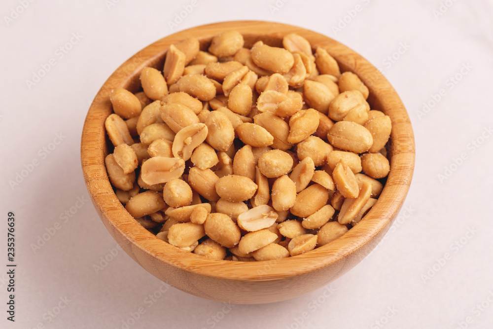 Roasted peanuts in wooden bowl on light marble background Roasted peanuts in wooden bowl on light marble background