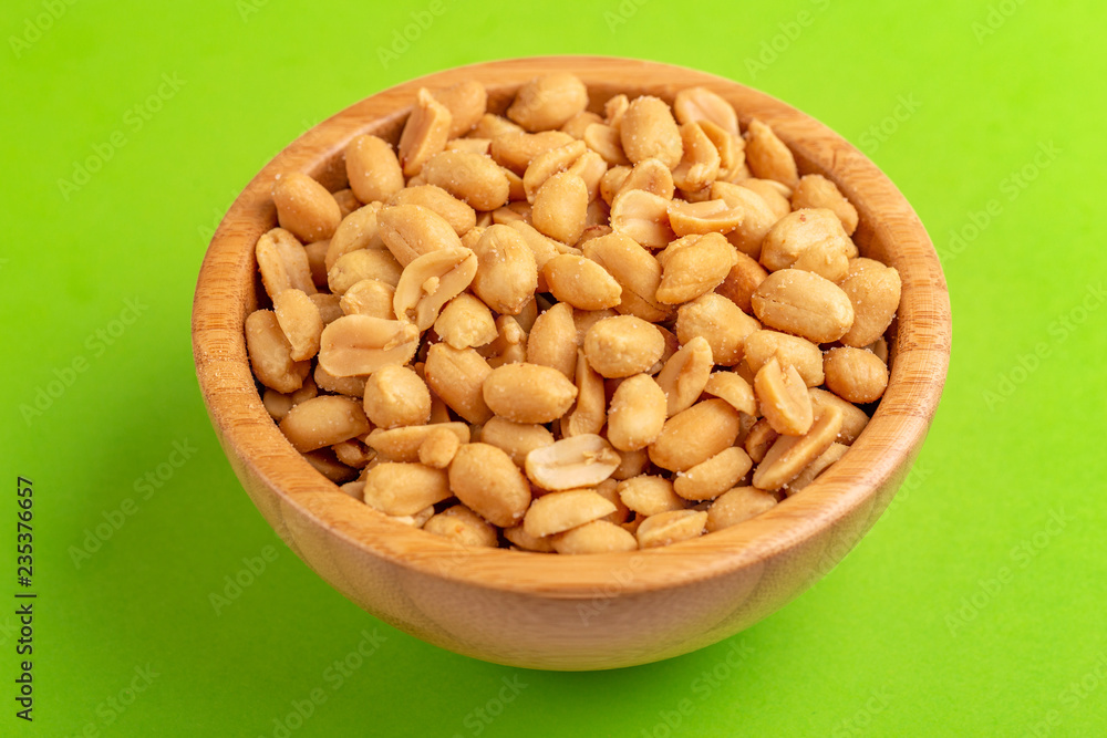 Roasted peanuts in wooden bowl on bright green background Roasted peanuts in wooden bowl on bright green background