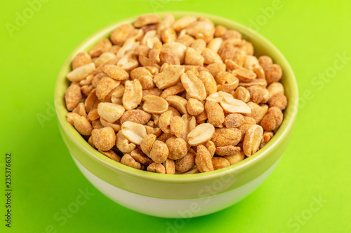 Roasted peanuts in bowl on bright green background