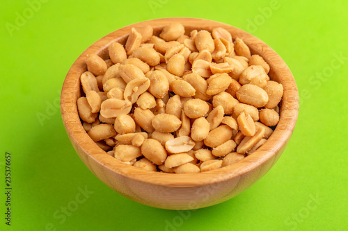 Roasted peanuts in wooden bowl on bright green background