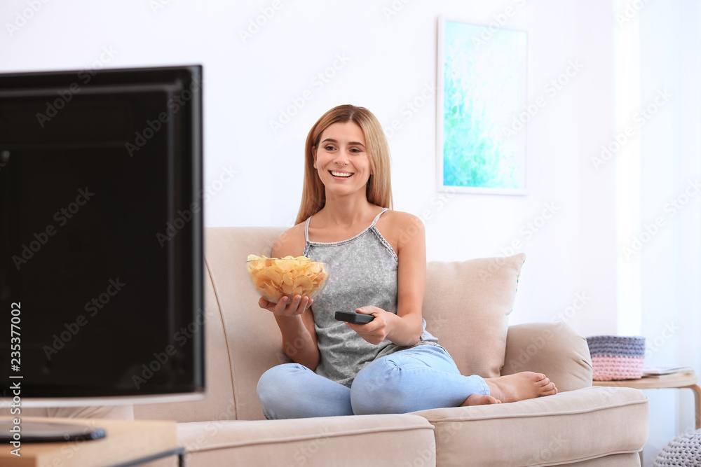 Woman with bowl of potato chips watching TV on sofa in living room Woman with bowl of potato chips watching TV on sofa in living room