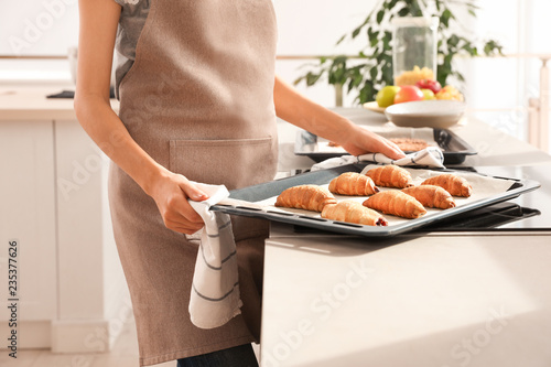 Young woman holding oven sheet with homemade croissants in kitchen, closeup