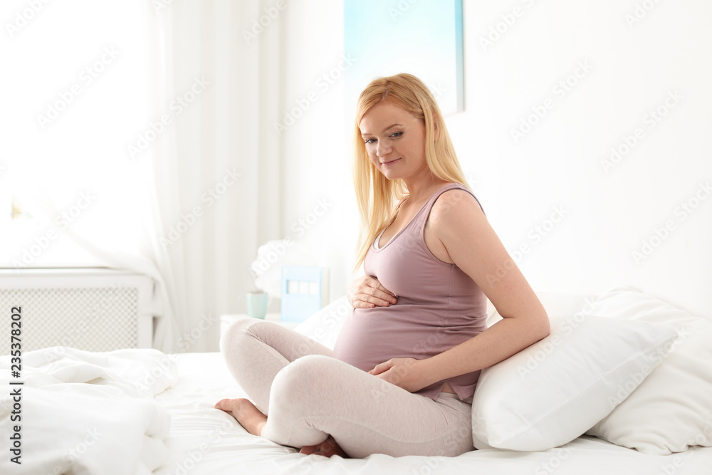 Pregnant woman sitting on bed in light room Pregnant woman sitting on bed in light room