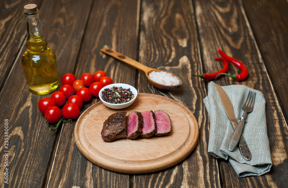 steaks, roast beef on the board with spices, tomatoes, chili pepper, on wooden background, top view