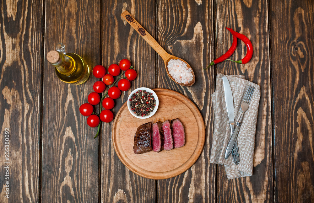 steaks, roast beef on the board with spices, tomatoes, chili pepper, on wooden background, top view