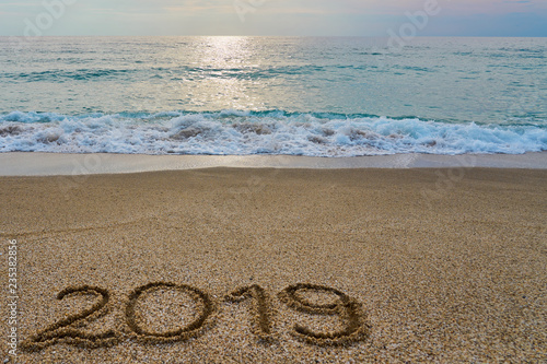 New year 2019 inscription written on the sand with waving sea on a sunset. Copy space. 
