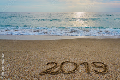 New year 2019 inscription written on the sand with waving sea on a sunset. Copy space. 