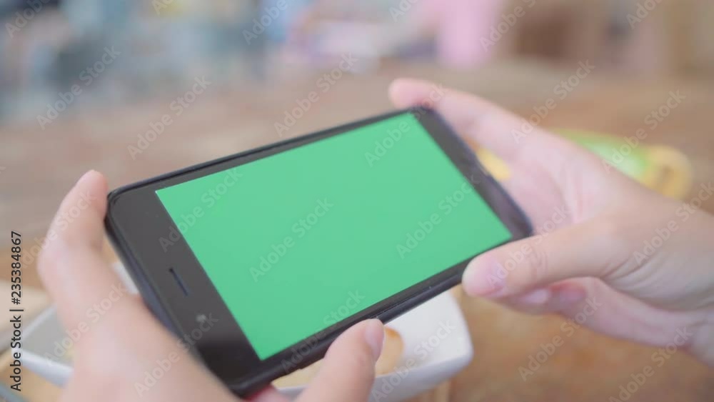 Young asian woman using black mobile phone device with green screen. Asian woman holding smartphone, scrolling pages while sitting in cafe. Chroma key. Young asian woman using black mobile phone device with green screen. Asian woman holding smartphone, scrolling pages while sitting in cafe. Chroma key.