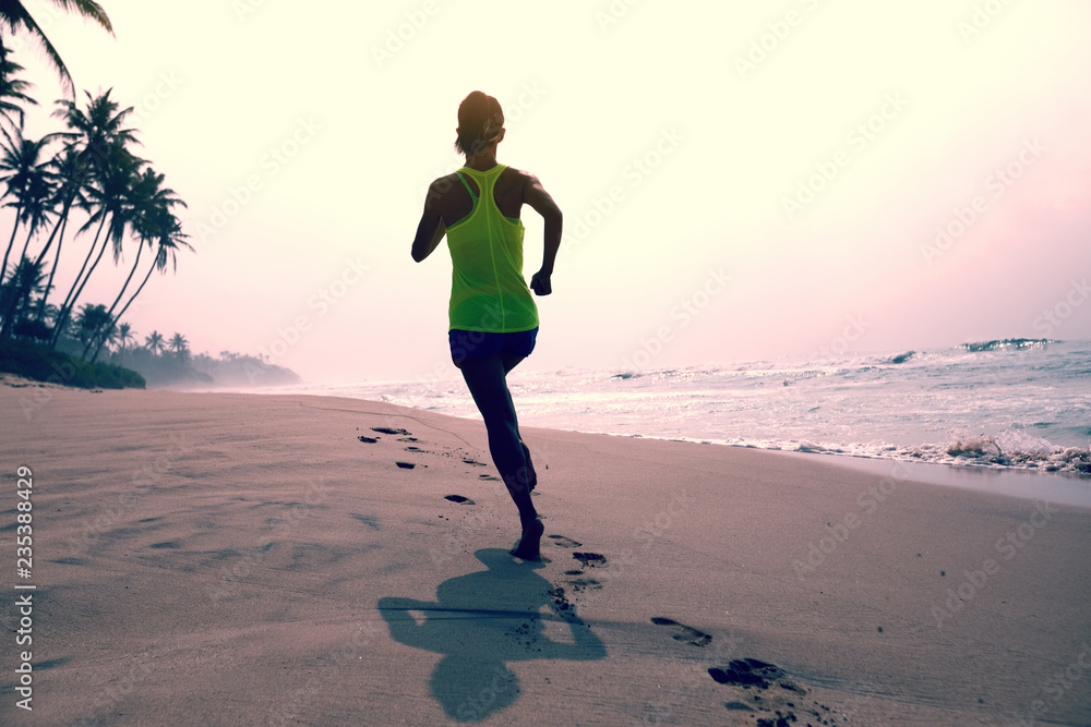 Fitness healthy lifestyle young woman running on tropical beach during sunrise in the morning