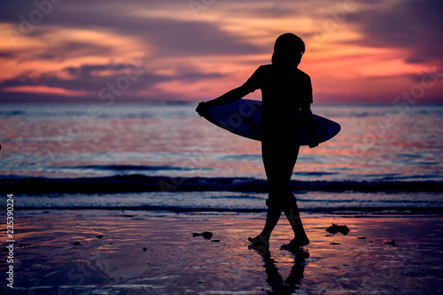 Silhouette of a surfer heading into the water during sunrise. Surfer at sunset time. Sunset on the beach with surfer watching waves.
