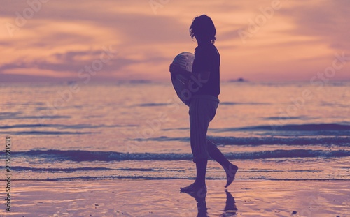 Silhouette of a surfer heading into the water during sunrise. Surfer at sunset time. Sunset on the beach with surfer watching waves.
