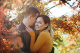 Young couple boy and girl hug and kiss in autumn park. Fall. Young Man and Woman outside. Happy family Concept. Yellow Trees and Leaves.