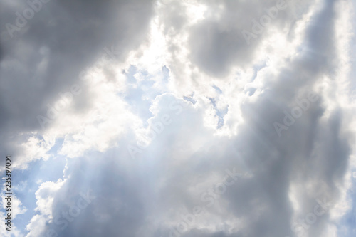 Clouds and sun shines through rays of light in the illuminated picturesque sky. Blue sky with clouds after the rain.