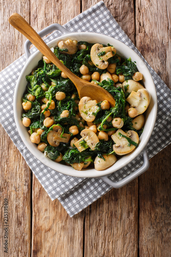 Stew of chickpeas with spinach and mushrooms close-up in a bowl. Vertical top view