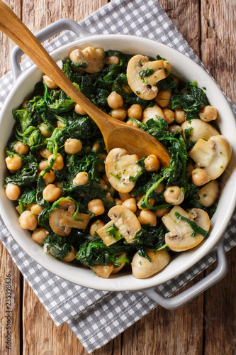 Delicious braised chickpeas with spinach and mushrooms closeup in a bowl. Vertical top view