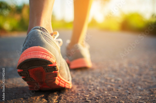 Feet of woman walking and exercise on the road during sunset.