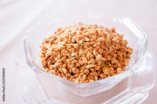 Glass bowl of roasted crushed peanuts isolated on white background.
