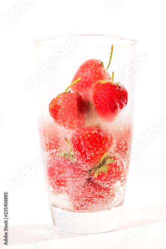 Pouring water on fresh strawberry with dancing bubbles in tall glass isolated on white background. 